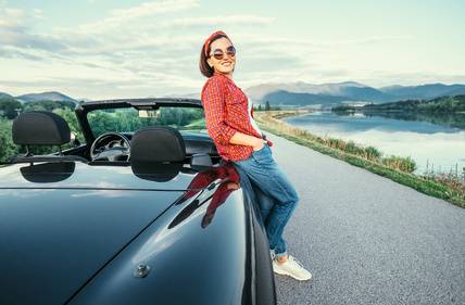 photo : Young woman stand near cabriolet car on the  road with beautiful mountain lake view