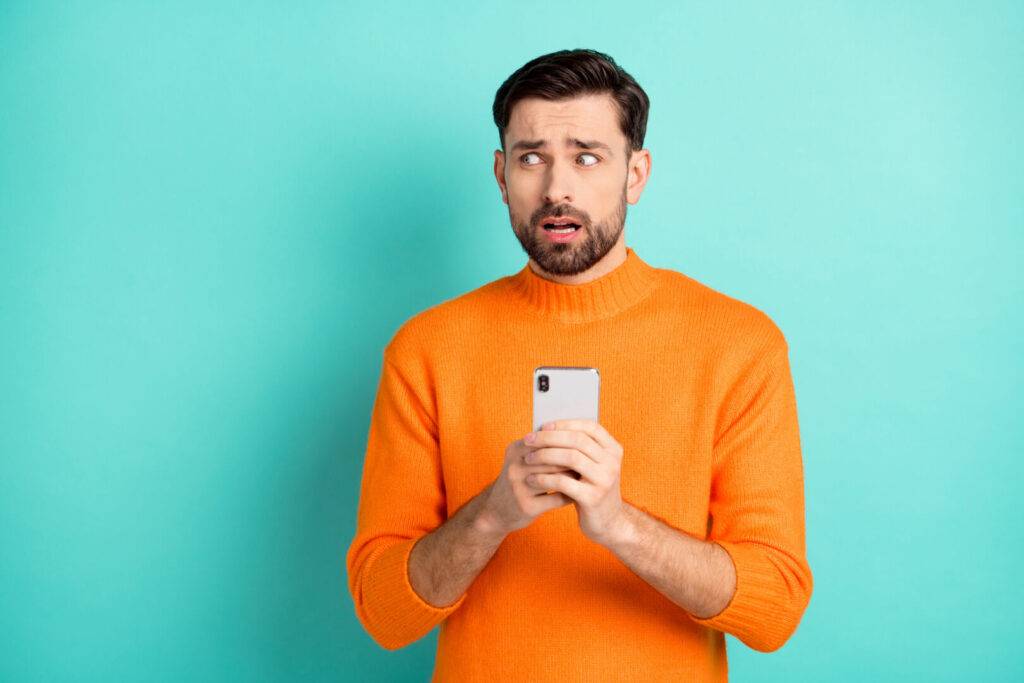 photo : Photo of young man afraid scared nervous use cellphone look empty space fail problem isolated over turquoise color background