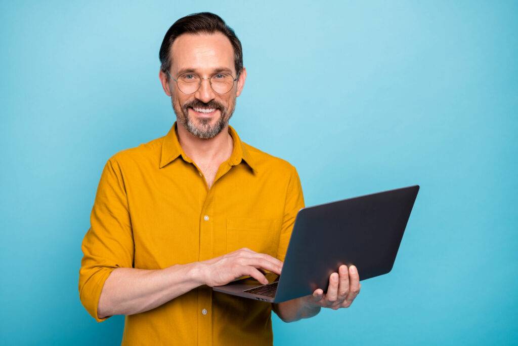photo : Portrait of positive cool mature man hold his computer work text type chatting with family colleagues wear good looking clothes isolated over blue color background