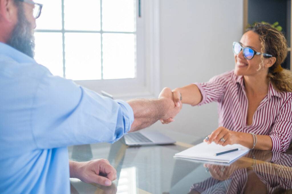 photo : Smiling caucasian female hr manager handshake hire male candidate at job interview make good first impression, happy mixed race client shake hand of bank broker, respect, business agreement concept.