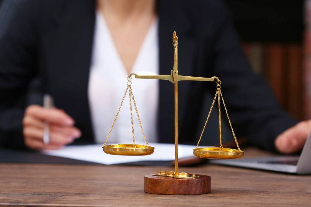 photo : Scales of justice on wooden table and female lawyer on backgroun