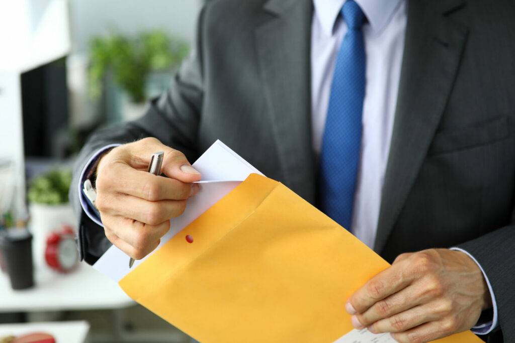 photo : Clerk in suit and tie at workplace packing envelope unpacking envelope with important documentation