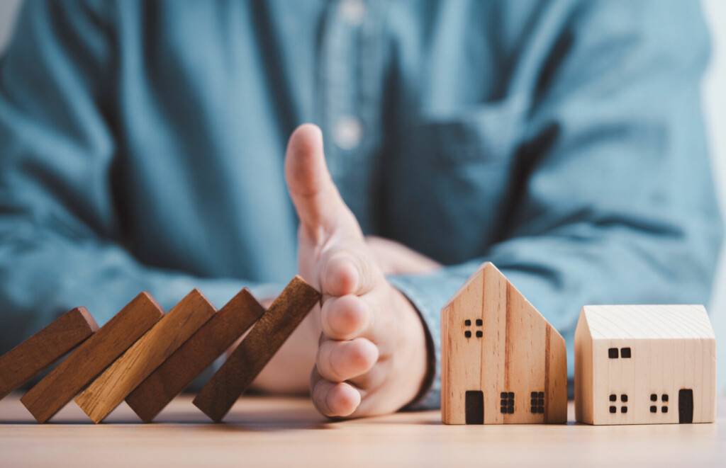 photo : Businessman hand protect and stop wooden house from domino falli