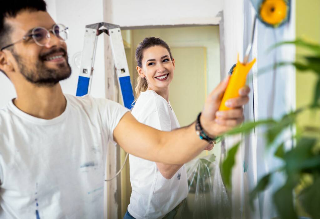 photo : Smiling young couple painting wall in their home.