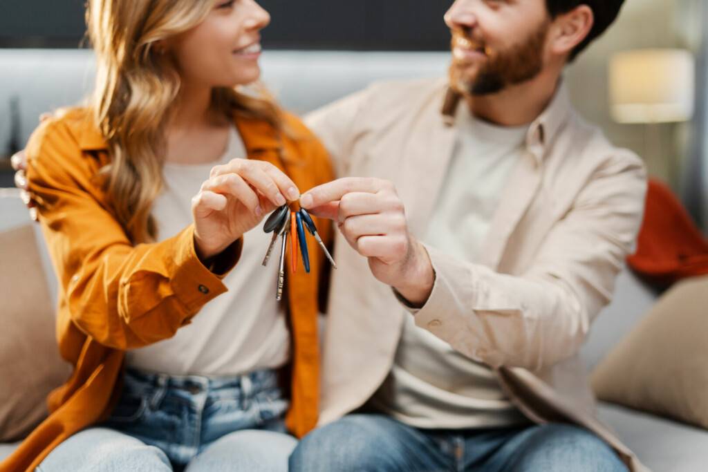 photo : Happy young family holding keys from new home, selective focus. Attractive smiling man and woman hugging buying new property sitting together on comfortable sofa. Moving concept