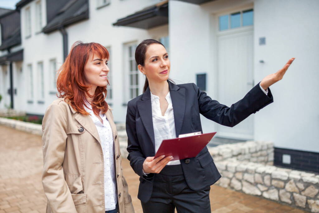 photo : Young woman with real estate agent visiting house for sale in residential area, copy space