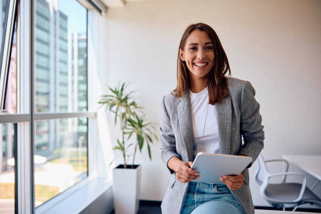 photo : Young happy businesswoman using touchpad while working in office and looking at camera.