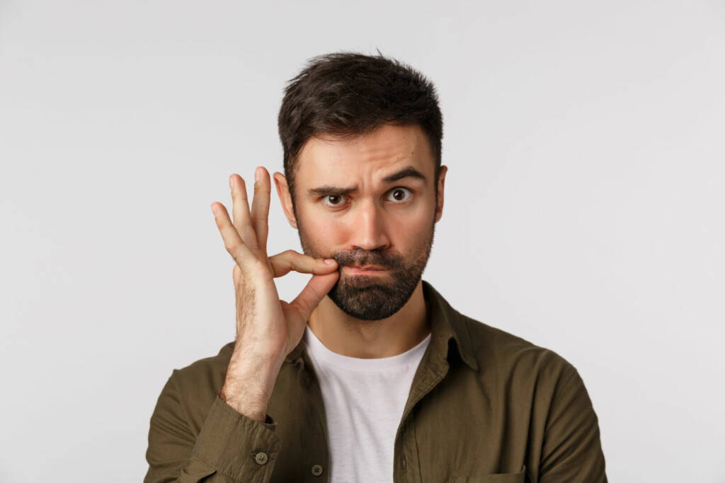 photo : My lips are sealed with promise. Serious and funny bearded adult man keep mouth shut, making zip gesture and raise one eyebrow as hinting person stay silent, keep secret safe, white background