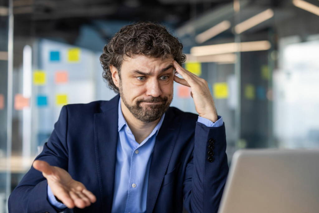 photo : Frustrated businessman sitting at office desk looking at computer screen with hand on head