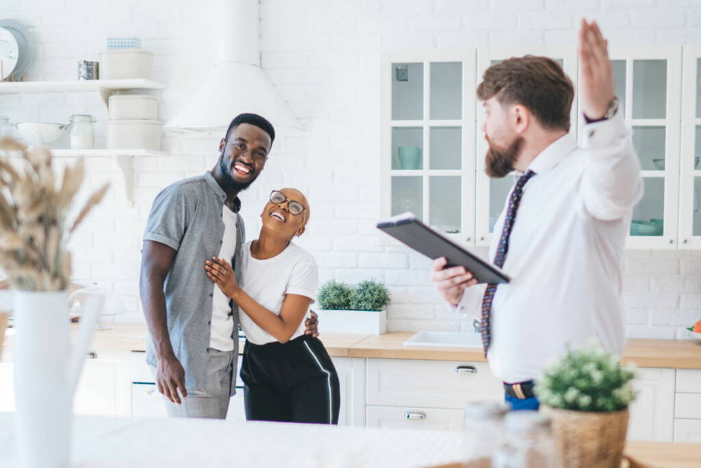 photo : Confident estate agent showing kitchen to African American elated couple