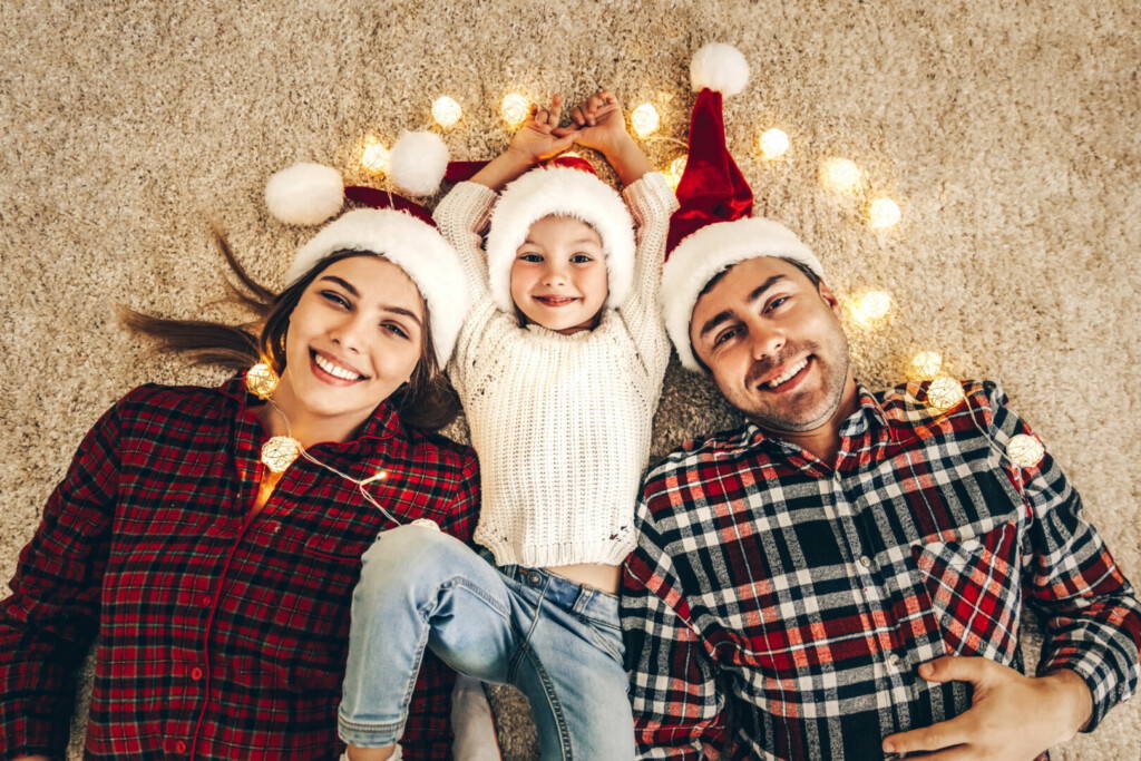 photo : Christmas. Family. Happiness. Top view of dad, mom and daughter in Santa hats looking at camera and smiling while lying on the floor at home