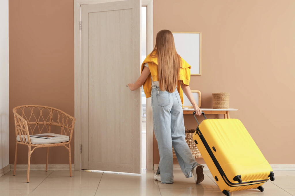 photo : Young woman with suitcase opening door in hotel room