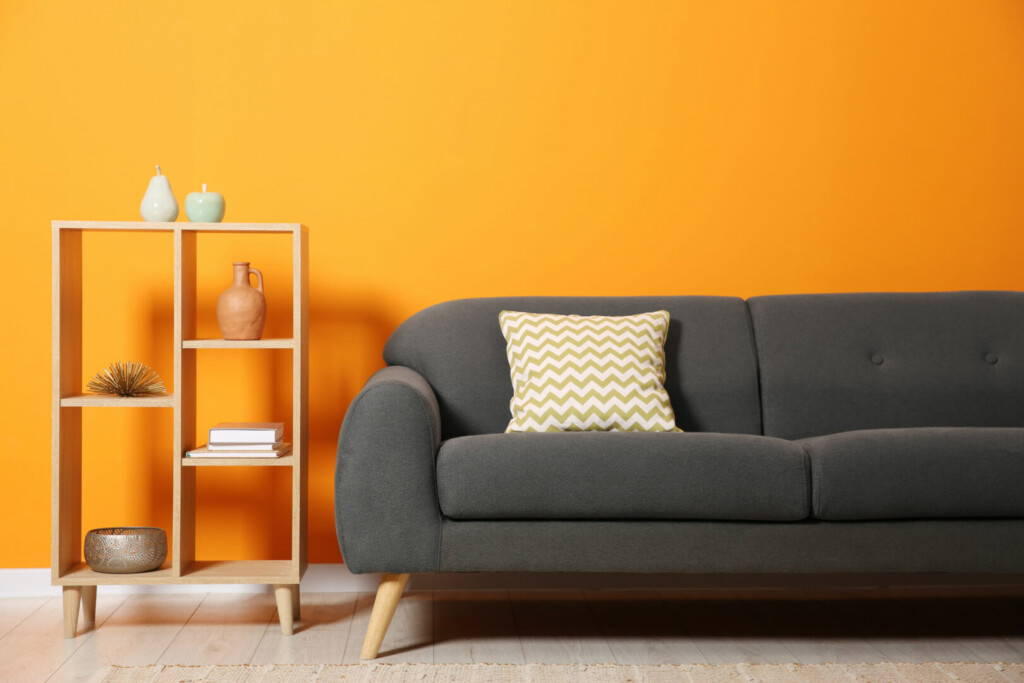 photo : Stylish sofa with cushion and decor elements near orange wall