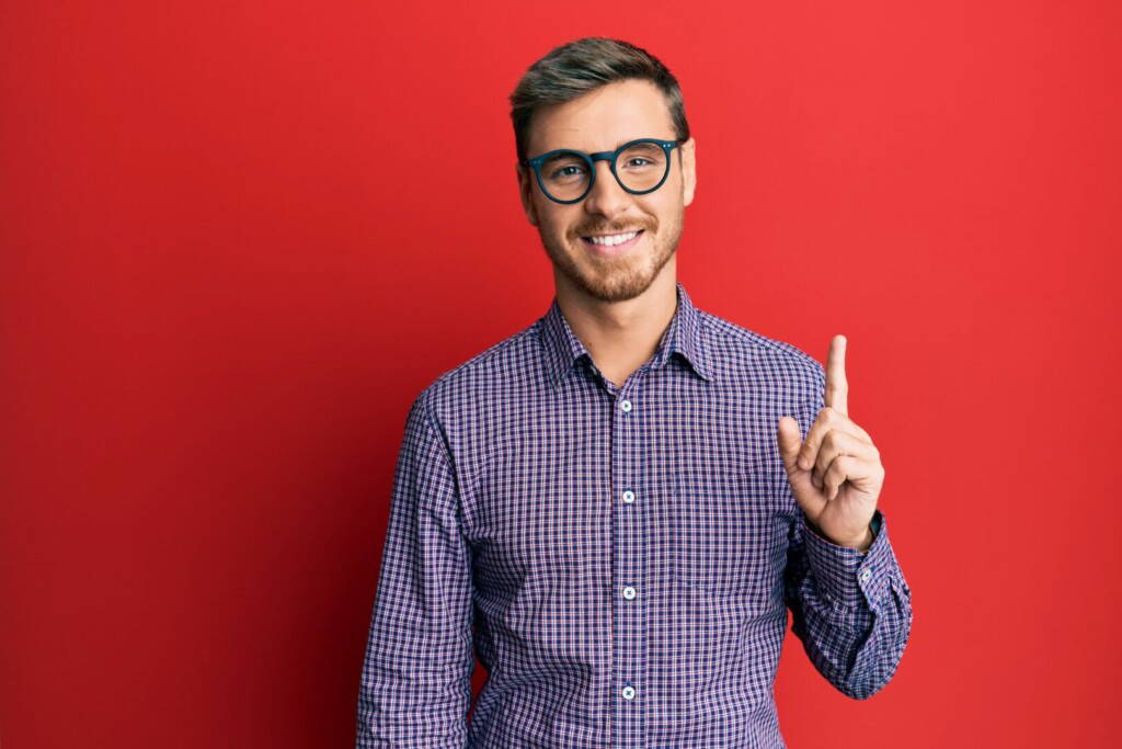 photo : Handsome caucasian man wearing business shirt and glasses smiling with an idea or question pointing finger up with happy face, number one