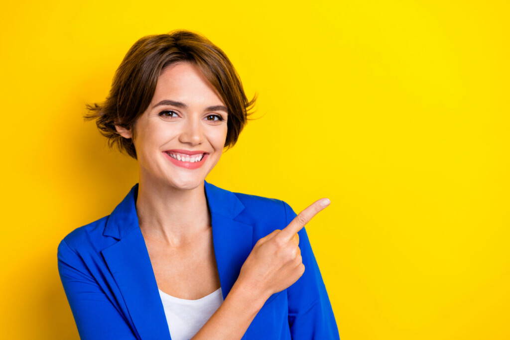 photo : Closeup portrait of positive charming businesswoman wear blue jacket office wear direct finger mockup useful tips isolated on yellow color background